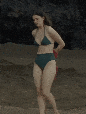 a woman in a green bikini is walking on the beach