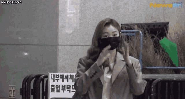 a woman wearing a mask and a suit is standing in front of a sign that says .