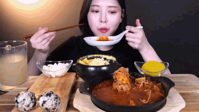 a woman is sitting at a table eating food with chopsticks and a spoon