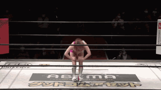 a woman in a pink bikini is kneeling in a wrestling ring with a sign that says abema on it