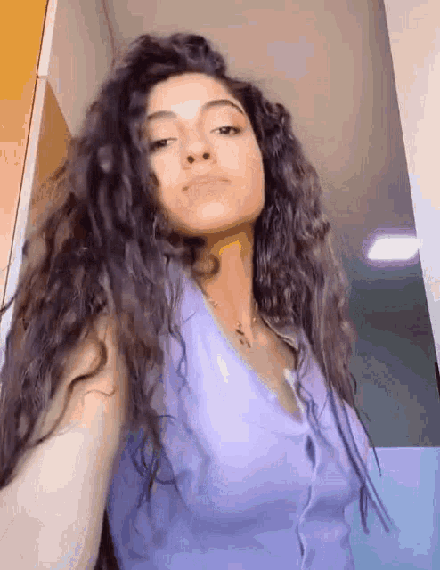 a woman with curly hair is taking a selfie in a purple tank top .