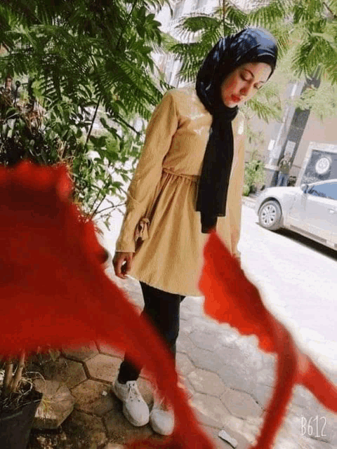 a woman wearing a hijab and a scarf is standing in front of a car .
