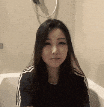 a woman sitting in a bathtub with a shower head hanging on the wall behind her