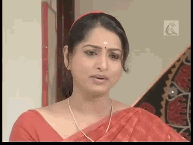 a woman wearing a red saree and a gold necklace looks at the camera