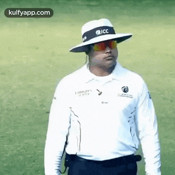 a man wearing a white hat and sunglasses is standing on a field .