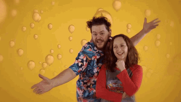 a man and a woman are posing for a picture with balloons and the letter t behind them
