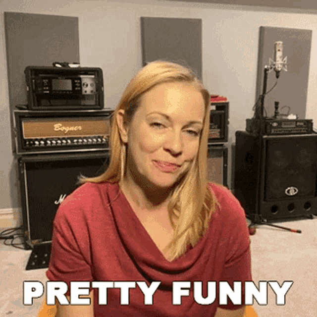 a woman in a red shirt says pretty funny in front of a stack of amps