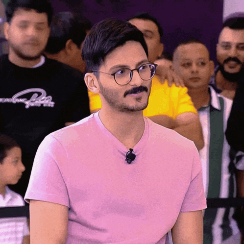 a man wearing glasses and a pink shirt has a microphone attached to his collar