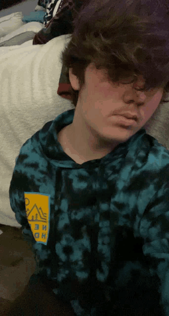 a person wearing a blue tie dye hoodie with a yellow square on the sleeve