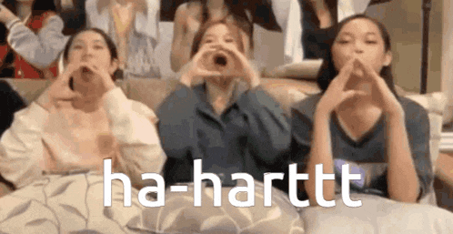 three young girls are sitting on a couch making a heart shape with their hands .