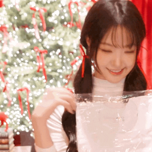 a woman with pigtails is smiling while holding a plastic bag in front of a christmas tree