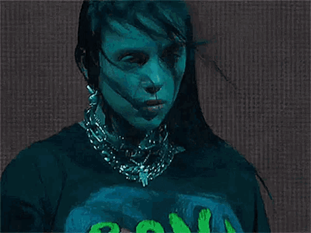 billie eilish is wearing a black t-shirt with a green logo on it and a chain around her neck .