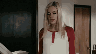 a blonde woman in a red and white shirt is standing in front of a printer .