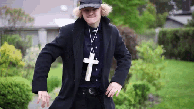 a man wearing a hat and a black coat has a cross around his neck