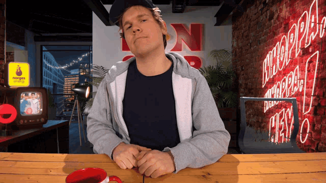 a man sitting at a table in front of a neon sign that says ' nn ' on it