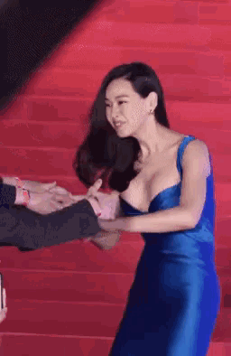 a woman in a blue dress is holding a man 's hand on a red carpet
