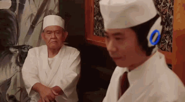 a man in a chef 's hat is standing next to an older man in a white robe .