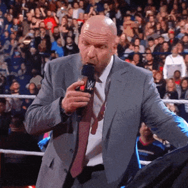a man in a suit and tie is speaking into a microphone with a wwe logo on it
