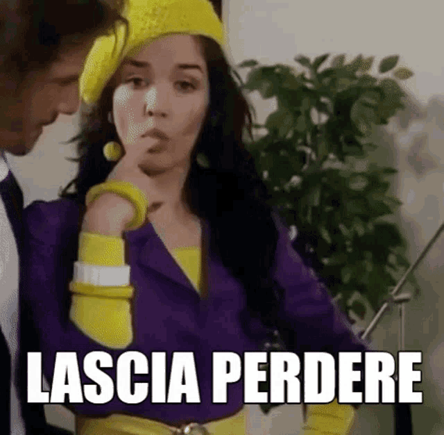 a woman wearing a yellow hat and a purple jacket is standing next to a man and the words lascia perdere are on the screen