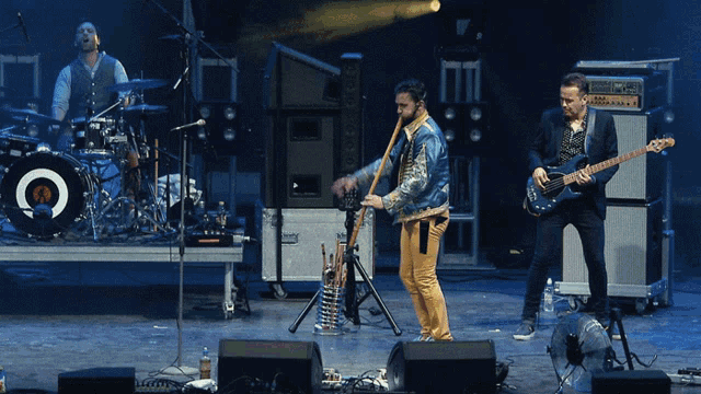 a man playing a guitar on a stage with a drummer and a man playing a flute