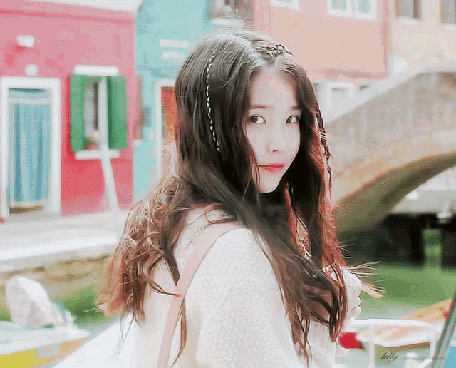 a girl with long hair is standing in front of a bridge and a building that says lilly on it