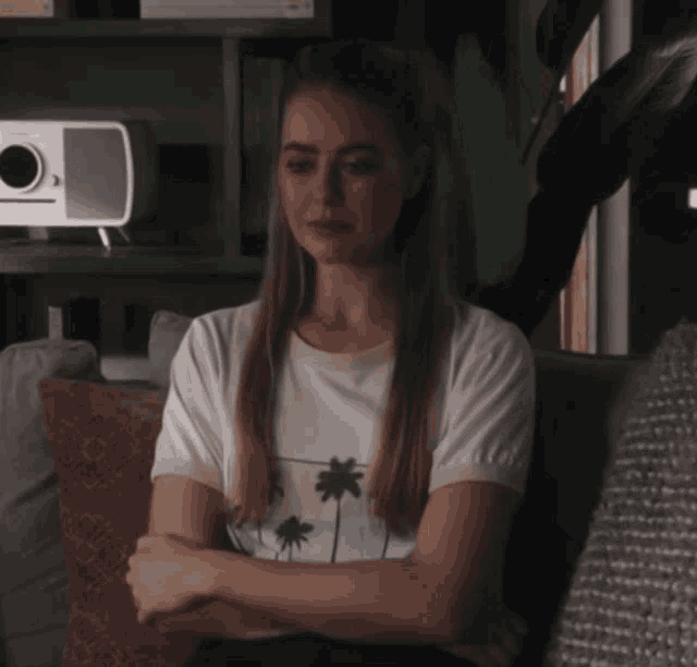 a woman in a white t-shirt with palm trees on it sits on a couch