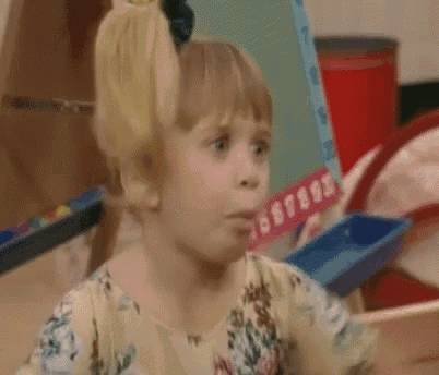 a little girl with a bow in her hair is making a funny face while sitting in front of a pile of toys .