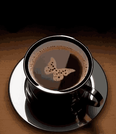 a cup of coffee with a butterfly on it is on a saucer on a wooden table .