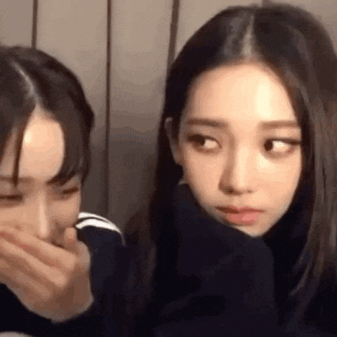 two girls are sitting next to each other and one of them is covering her mouth .