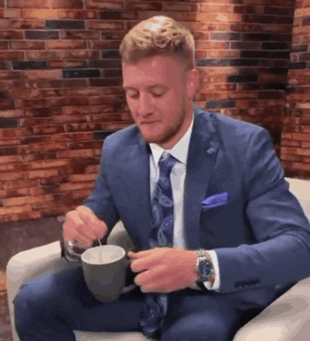 a man in a suit and tie is sitting in a chair holding a cup of coffee