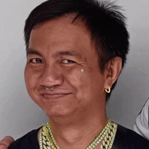 a man wearing a gold chain and earrings is smiling .