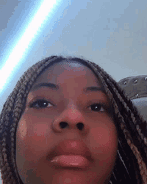 a close up of a woman 's face with braids and a light shining on her face .