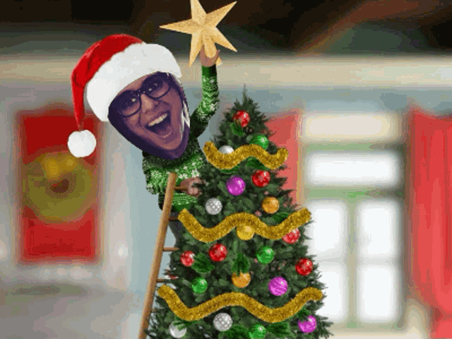 a man wearing a santa hat is holding a star above a christmas tree