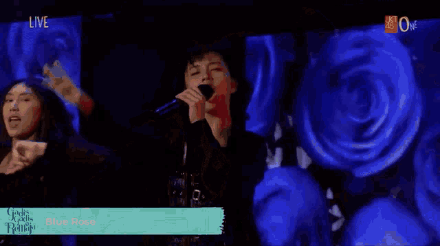 a man singing into a microphone in front of a blue rose background