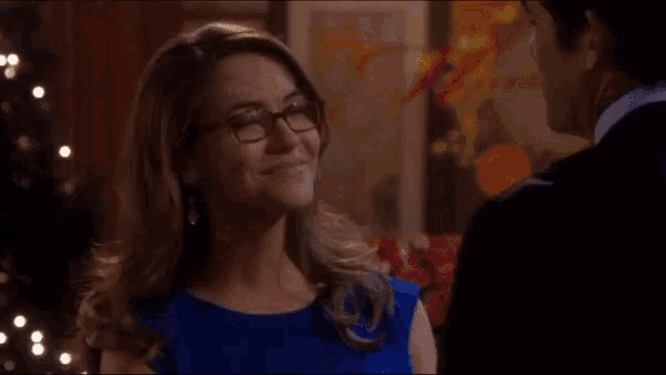 a woman wearing glasses and a blue dress is smiling at a man