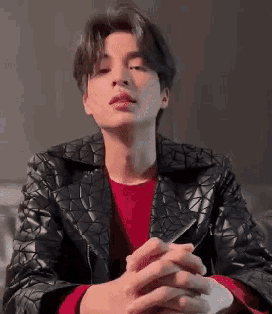 a young man wearing a black leather jacket and a red sweater is sitting on a couch .