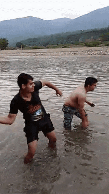 two men are standing in a body of water with one wearing a shirt that says ' adidas ' on it