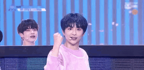 a boy in a pink sweater is making a fist in the air while another boy looks on .