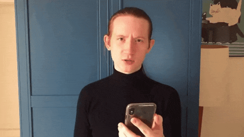 a woman in a black turtleneck holds a cell phone in front of a blue door