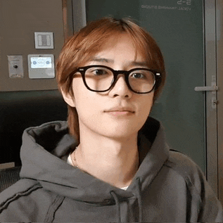 a young man wearing glasses and a grey hoodie is looking at the camera .
