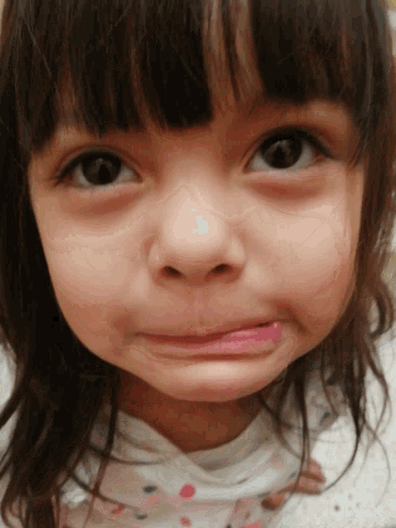 a close up of a little girl 's face with a white shirt on