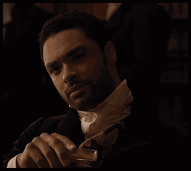 a man in a tuxedo and tie is holding a glass of whiskey .
