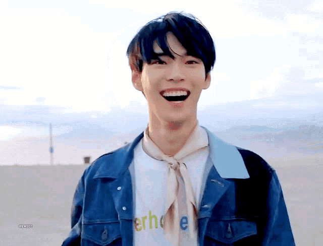 a young man wearing a denim jacket and a white t-shirt with the word erh on it is laughing .