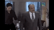 a man in a suit and tie is walking in a room with a woman .
