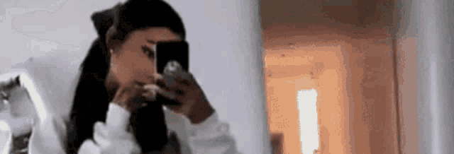 a woman is taking a selfie in front of a mirror with her phone .