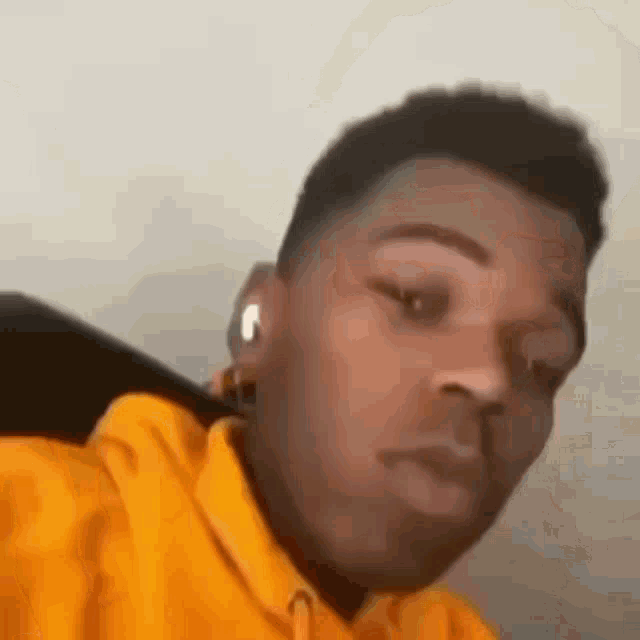 a young man wearing a yellow hoodie and ear buds is taking a selfie .