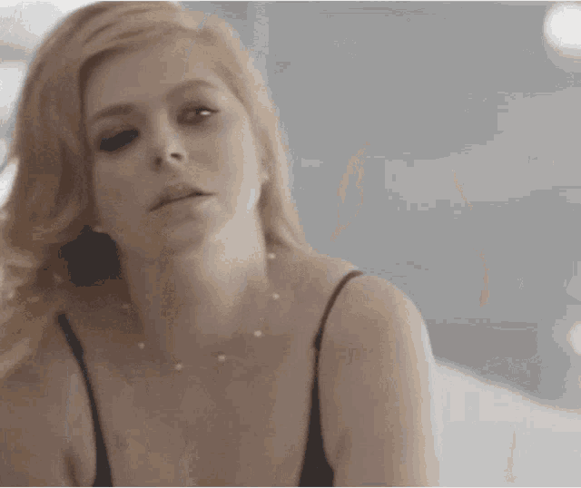 a woman in a black tank top and pearl necklace looks at the camera