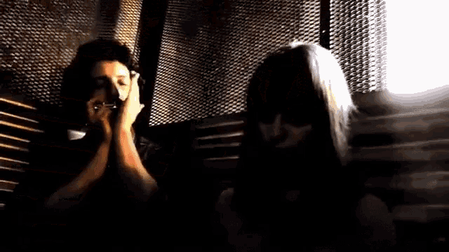 a man and a woman are sitting next to each other in a dark room . the woman is covering her mouth with her hands .