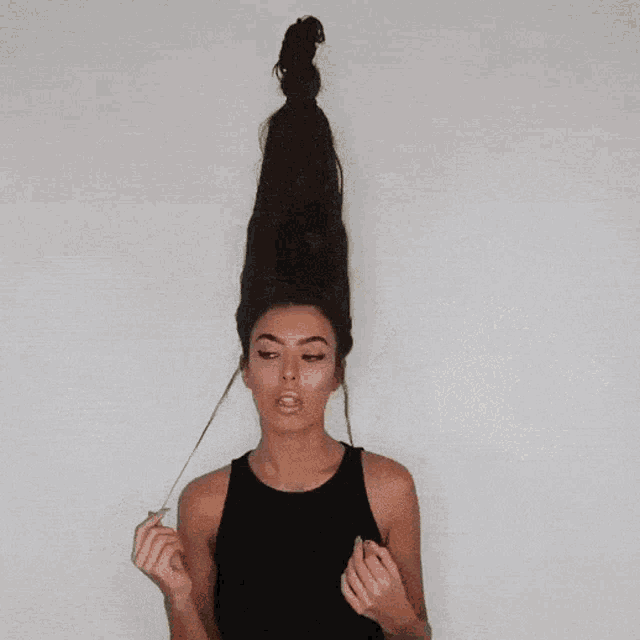 a woman with very long hair in a bun is wearing a black tank top