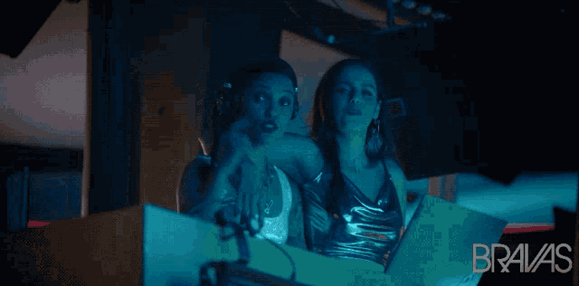 two women are sitting in front of a laptop and the word bravas is on the bottom
